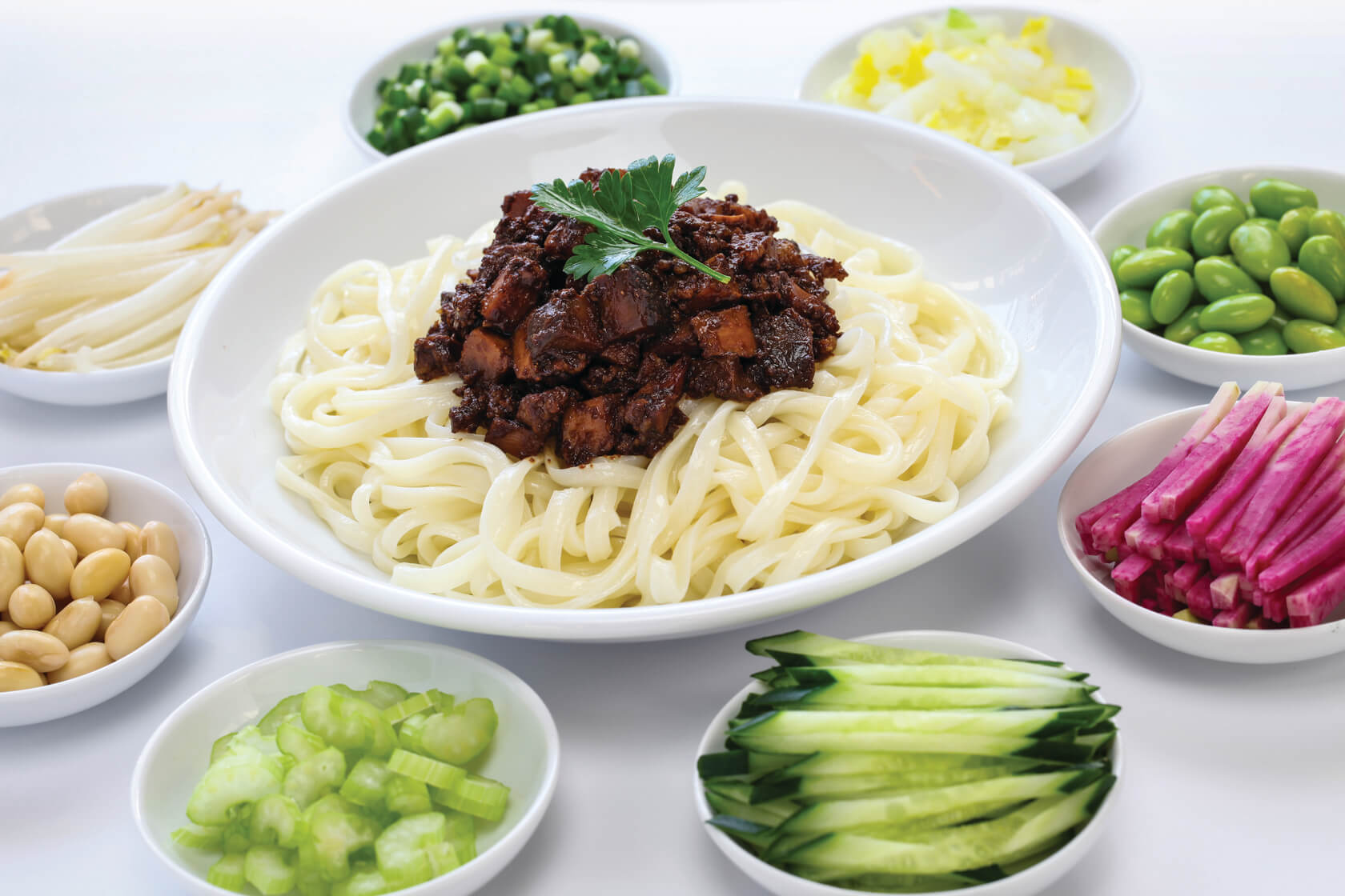 Beijing Fried Sauce Noodles in a bowl surrounded by an assortment of topings
