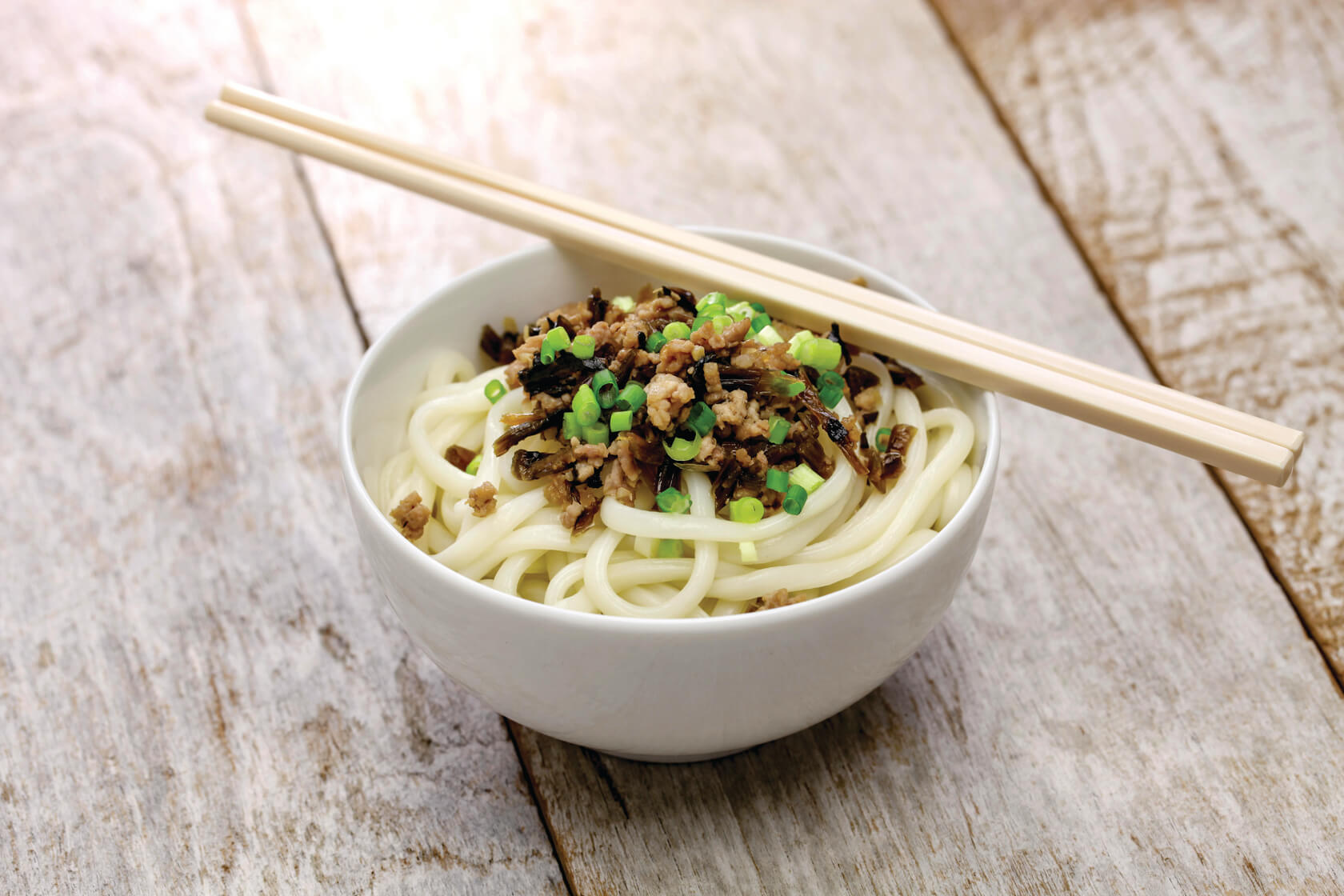 A bowl bowl of Sichuan DanDan Noodles with a pair of chopsticks resting on top 