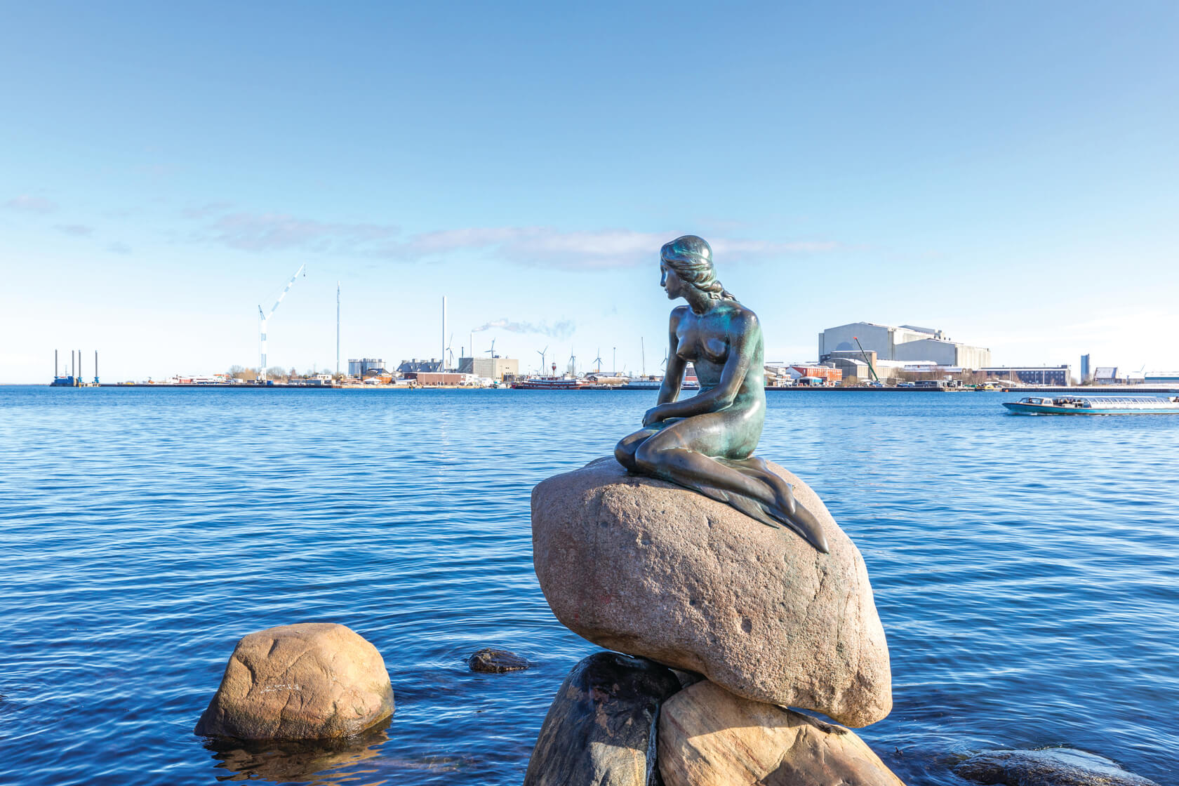 An iron sculpture of a mermaid resting on a rock overlooking the Copenhagen bay
