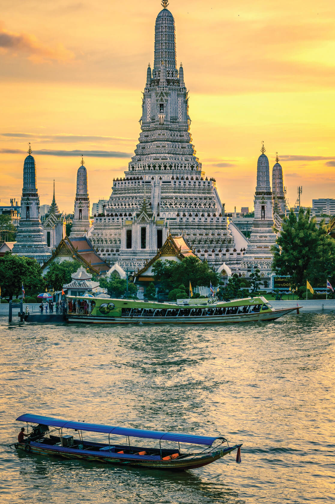 Temple of the Emerald Buddha in front of a golden sky and behind a calm body of water