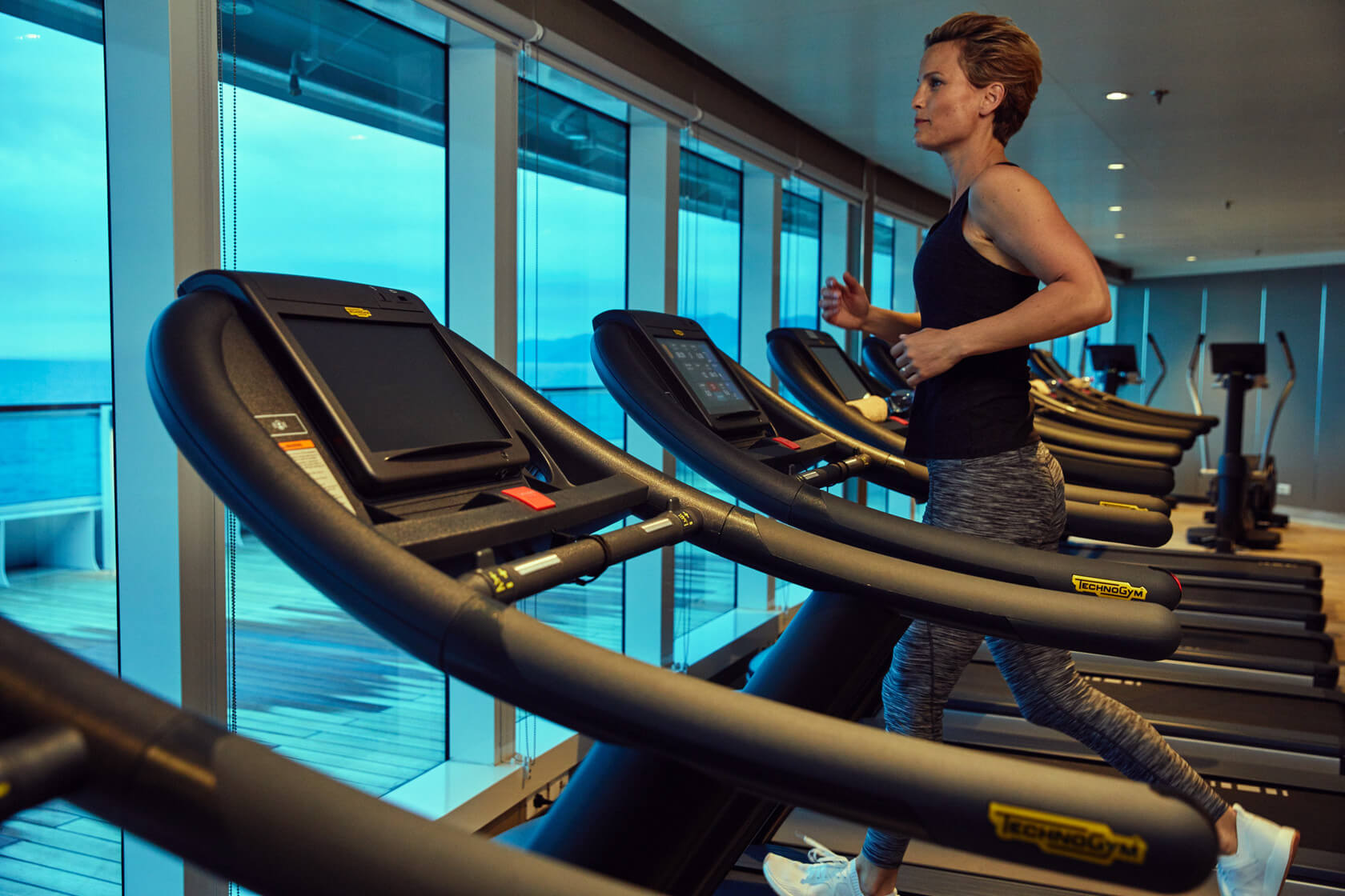 A women on a treadmill inside the Seabourn gym looks out into the ocean view.