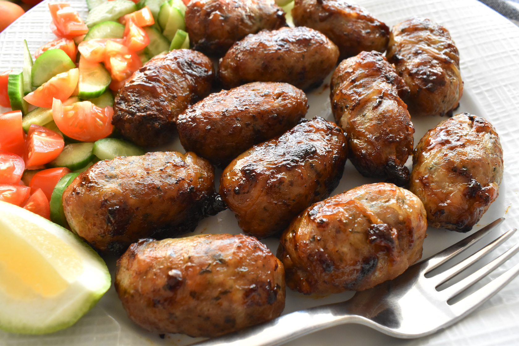 Sheftalia : Cypriot Lamb and Pork Sausages. Grilled Sausages with Fresh Vegetables (Cucumber and Tomato) on a White Plate. Traditional Cypriot food.